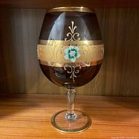 Front side of the amethyst Bohemian snifter showing gold band and floral enamel decoration on dark purple glass.