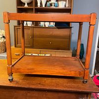 Front view of the wooden two-shelf bar cart showing its rectangular shape and casters.