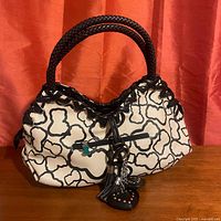 Front view of black and white patterned leather purse with woven black leather handles and small green bear zipper pull on front pocket zipper