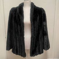 Front view of the black faux fur coat on a dress form against a plain background.