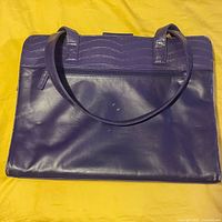Top view of closed purple leather rectangular briefcase with croc pattern handles and top edges