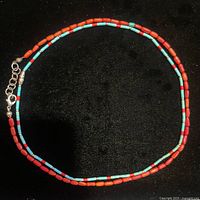 Full view of one Navajo necklace showing turquoise, coral, and silver beads on black background.