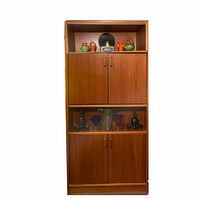 Front view of tall Danish teak storage cabinet with two closed cabinets and two open shelves displaying decorative items.