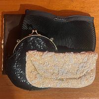 Four vintage clutches arranged; cream beaded sequin clutch, black shell bead clutch, black satin clutch with folded details, faded black clutch