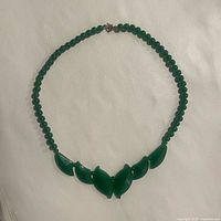 Full view of the necklace laid flat, displaying the round green quartz beads and the carved jade leaf centerpiece.