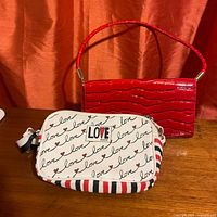 Canvas LOVE Brighton purse with red, white, and blue script love and heart pattern, adjustable strap, and red embossed leather purse with crocodile texture and matching handle on a wood and fabric background