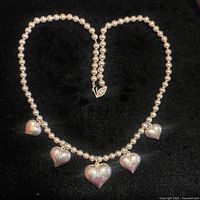 Front view of sterling silver necklace with silver bead chain and five puffed heart-shaped charms on black background.