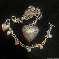 Photo showing the full bracelet with five small heart charms and toggle clasp alongside the necklace with large double-sided heart pendant and chain.