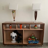 Front view of the wooden media shelf with three smaller cubbies on top and two larger cubbies below, displaying various decorative pottery and a bust statue, with two lamps on top.