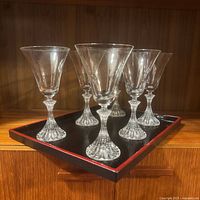 Six Mikasa Stratton stemware glasses arranged on black faux bois tray with red striping on wooden shelf