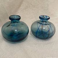 Front view of the pair of blue striped hand blown glass bud vases on a neutral fabric surface.