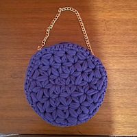 Front view of round handwoven purple knit purse showing floral knit pattern and gold chain handle.