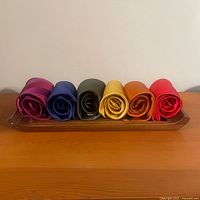 Front view of six rolled silk ties arranged on a handmade wooden tray