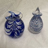 Two studio art glass pieces, a blue feathered bud vase and a blue feathered perfume bottle with stopper, on a light fabric background.