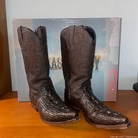 Pair of men's dark brown leather cowboy boots with textured toes and patterned shafts, standing in front of original Texas Legacy box on wooden surface.