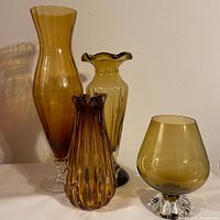 Three hand blown amber glass vases and one amber snifter arranged side by side showing shape, color, and size differences.