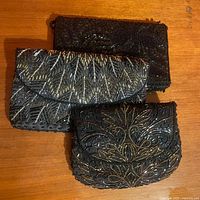 Overall view of all three vintage black beaded clutches stacked on a wooden surface, showing the different bead patterns and textures.