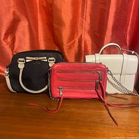 Photo showing all three leather handbags together: black Kate Spade, red Rebecca Minkoff, and ivory Strathberry