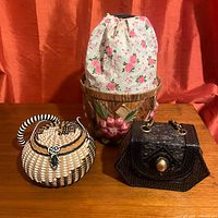 Three wicker purses together on a wooden surface with red-orange background. Includes black hexagonal purse with gold chain, floral basket purse and round floral embroidered purse.