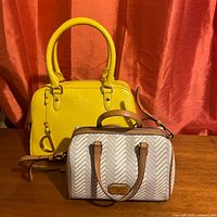 Both purses displayed side by side on a wooden surface with a red textured curtain background.