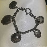 Front view of the vintage bracelet showing four lockets attached on a silver tone chain and one starburst charm