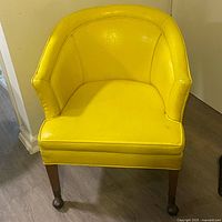 Front view of yellow naugahyde club chair showing upholstery and walnut legs with front ball casters