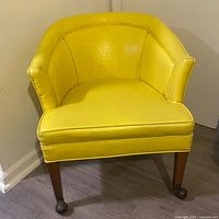 Front view of yellow Naugahyde club chair showing rounded back and visible wear on upholstery.