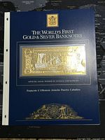 Blue presentation folder with gold and silver foil banknote mounted, labeled as "The World's First Gold & Silver Banknotes."
