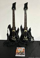Front view of two black Wireless Guitar Hero III guitar controllers and Guitar Hero III Wii game case.