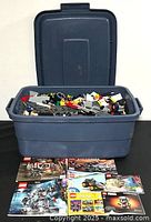 Blue Rubbermaid container open, showing assorted loose Lego pieces inside with instruction manuals displayed in front.