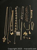 Photo of assorted gold tone necklaces, bracelets, pendants, and earrings laid out on black background showing condition and variety.