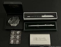 Overview of the pens, business card holder, and a glass or acrylic paperweight in black presentation boxes and foam inserts.