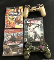 Photo showing three PlayStation 2 game cases: ‘‘Ultimate Ninja’’, ‘‘MLB 08 The Show’’, and ‘‘MX vs. ATV Unleashed’’, alongside two DualShock 4 wireless controllers in gold and camouflage colors.
