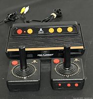 Atari Flashback 4 console with 2 joystick controllers and AV cables, showing front view with buttons and console design.