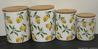 Front view of the 4 ceramic canisters with lemon designs and wooden lids, showing their different sizes.