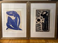 Photo of both framed prints together showing one blue figure and one black figure print in wood frames