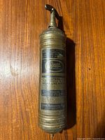 Full top-down view of the antique brass fire extinguisher showing the label with usage instructions and the curved top handle.