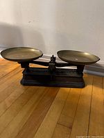 Front view of antique cast iron balance scale showing dual brass weighing pans on either side of cast iron base.