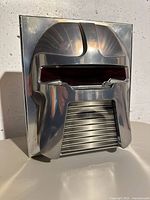Photo of the shiny silver metallic special edition packaging shaped like a Cylon head helmet with red visor detail.
