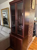 Tall brown wood cabinet with glass doors on upper half and wood doors on lower half.