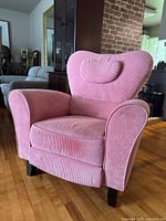 Front angled view of pink ribbed plush maternity rocker recliner with padded headrest and armrests, wooden legs.