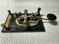 Close-up of the J-38 Morse code telegraph key showing the metal base and brass components with the plastic paddle and knob.