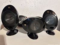 Five KEF black oval satellite speakers positioned on stands, showing front drivers and overall design.