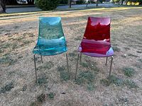 Front view of red and green translucent plastic chairs set on dry grass with metal legs visible.