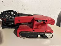 Side view of red Skil belt sander with power cord coiled beside it