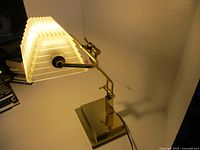 Lamp illuminated, brass arm, pleated glass shade, square base visible