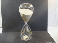 Full view of glass hourglass showing white sand and gold rings