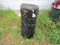 Full side view of black vinyl punching bag standing upright on ground, showing exterior wear and chain attachment