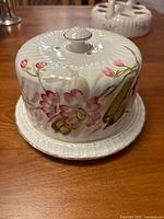 Front view of the antique covered porcelain dish showing pink and green floral design and ribbed base.