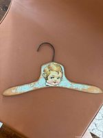Front view of the antique children's wooden hanger showing painted child's face and metal hook.